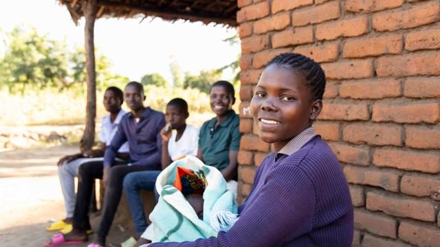 Ung afrikansk jente som holder en baby smiler til kameraet.