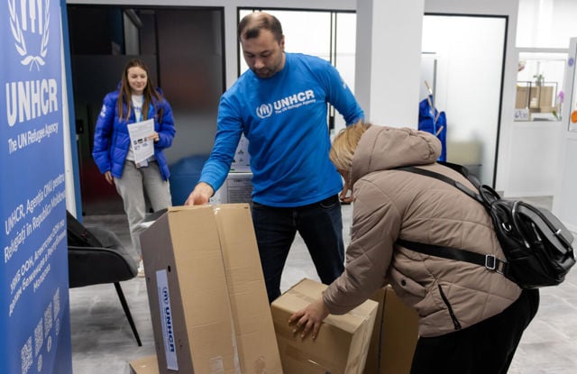 Man in UNHCR sweatshirt helps women move boxes.