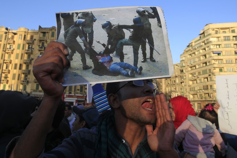 An Egyptian protester holds the widely seen image of Egyptian helmeted troops beating a veiled woman after having ripped her clothes off to reveal her bra and stomach during recent clashes, at a demonstration against the military rule in Cairo's Tahrir Square on December 22, 2011. AFP PHOTO/MOHAMMED ABED