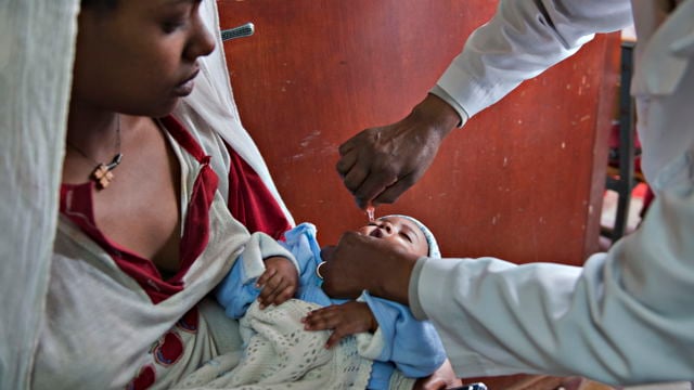 denne En helsearbeider gir en baby medisin med dråpeteller, mens barnet sitter på fanget til en voksen.